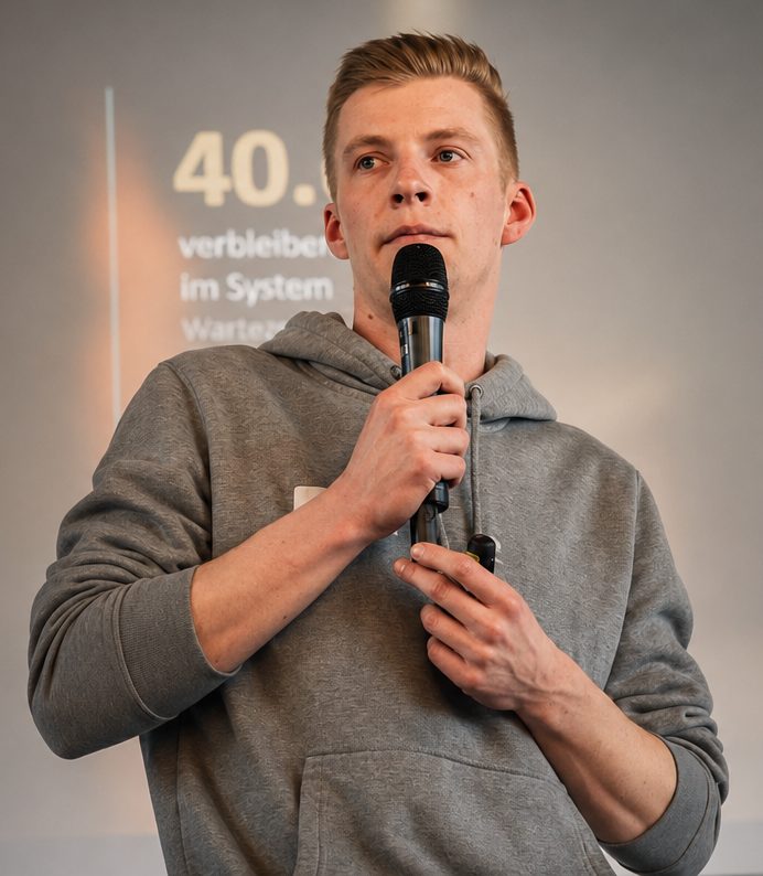 Foto: Hendrik Sichert spricht bei einem Vortrag, das Mikrofon in der Hand, hinter ihm eine Präsentation.